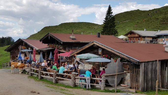 Das Bild zeigt die Stöfflhütte mit Terrasse auf der Menschen sitzen
