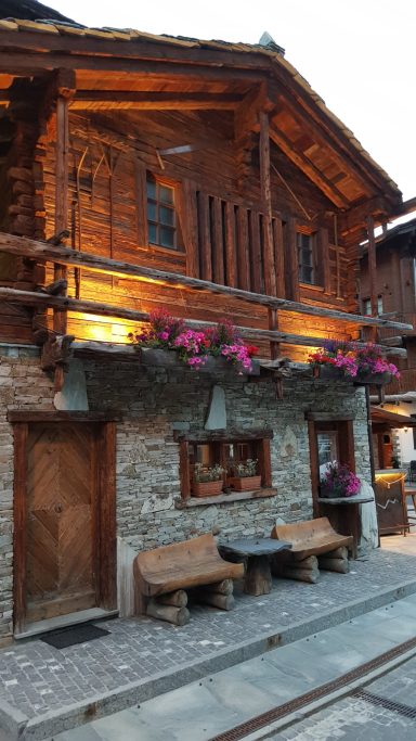 Ein beleuchtetes Holzhaus in Zermatt. Bänke stehen davor.